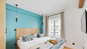 A modern hotel room with a large bed, a wooden headboard, and a view of the city through a window.