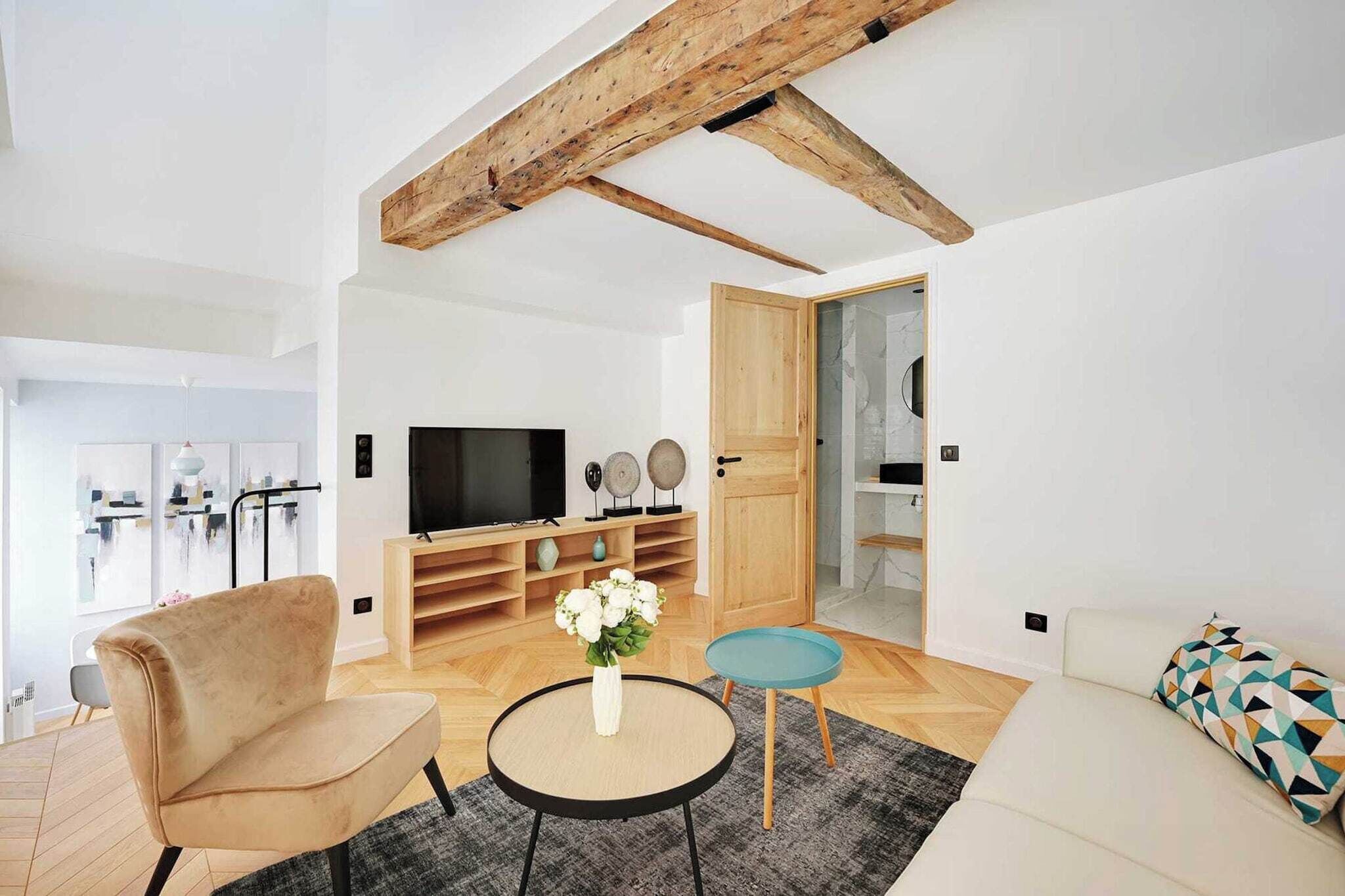 A modern living room with a wooden ceiling, a sofa, a TV, and a small table with a vase of flowers.