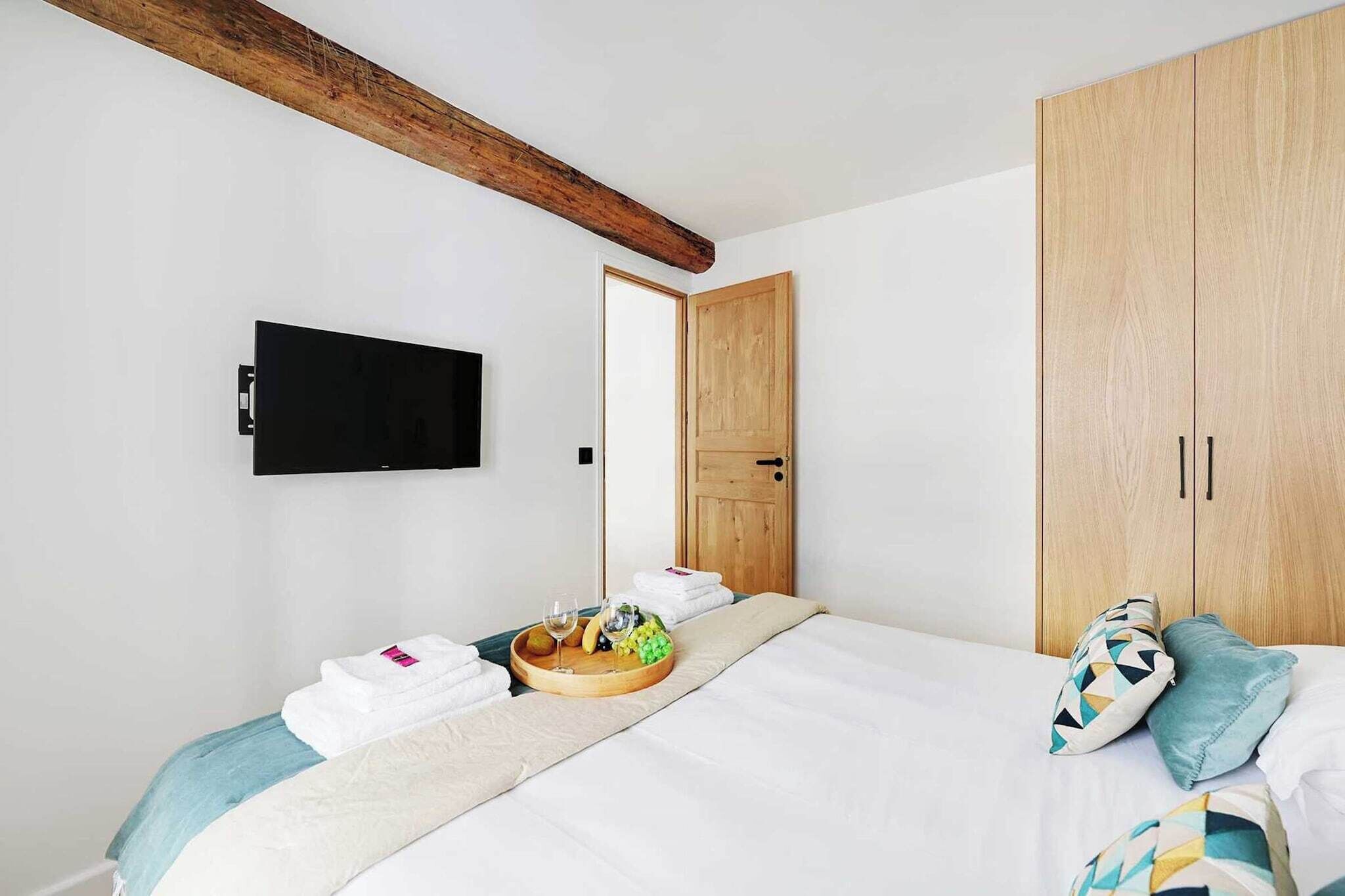 Ein Hotelzimmer mit einem Bett, einem Holzschrank, einem an der Wand montierten Fernseher und einem Tablett mit Früchten und Gläsern auf dem Bett.
