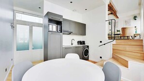 A modern kitchen with grey cabinets, a built-in microwave, and a washing machine. There is a round dining table with chairs.