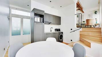 Une cuisine moderne avec des meubles gris, un four à micro-ondes encastré et un lave-linge. On y trouve une table de salle à manger ronde, accompagnée de chaises.