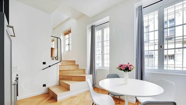 A modern interior with a staircase, a round dining table with chairs, and a vase of flowers.