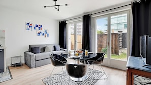 Ein modernes Wohnzimmer mit einem grauen Sofa, einem Esstisch mit vier Stühlen und einem Fernseher auf einem Holztisch.