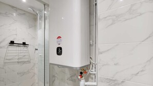 A bathroom with a glass shower enclosure, a white tiled wall, and a visible water heater with a control valve.
