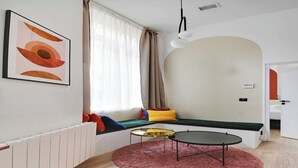 Ein modernes Wohnzimmer mit einer Couch, zwei kleinen Tischen, einer Heizung und einem Fenster mit Vorhängen.