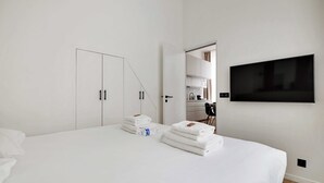 Ein modernes Hotelzimmer mit einem großen Bett, einem flachbildfernseher an der Wand, einem Schrank mit Spiegel und einer Küchenzeile.