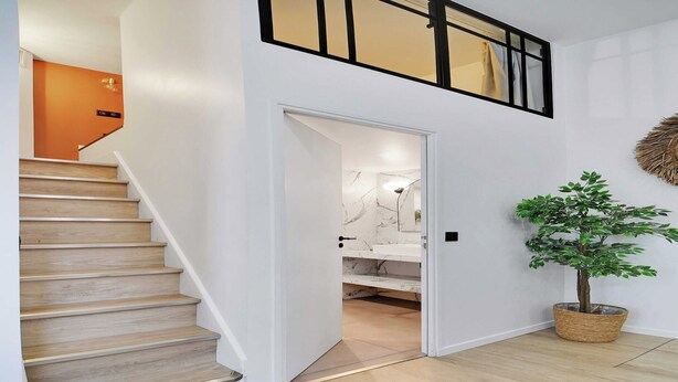 Eine Treppe führt zu einer zweiten Etage mit modernem Design, einer Topfpflanze und einer Marmorwand im Hintergrund.