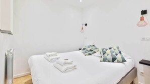 A modern hotel room with a neatly made bed, a radiator, a wall-mounted light fixture, and a power outlet. - Classy apartment in the heart of Le Marais (Paris)