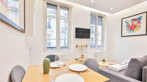 A modern dining area with a wooden table set for four, a cactus decoration, and a grey sofa in the background. - Classy apartment in the heart of Le Marais (Paris)