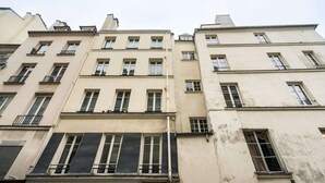 A row of multi-story buildings with uniform architectural style, featuring balconies and large windows. - Classy apartment in the heart of Le Marais (Paris)