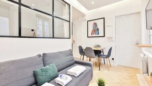 A modern living room with a grey sofa, a dining area with a table and chairs, and a large window. - Classy apartment in the heart of Le Marais (Paris)