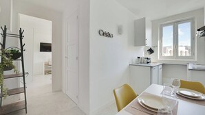 Une cuisine moderne avec des meubles blancs, une fenêtre et un coin repas avec une table mise pour deux personnes.