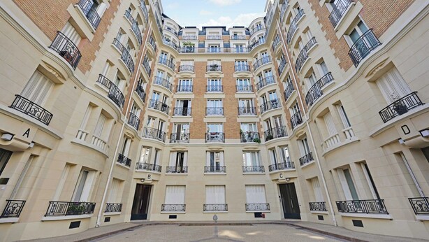 Un immeuble résidentiel à plusieurs étages, doté de balcons, d’une cour intérieure et d’une façade symétrique.