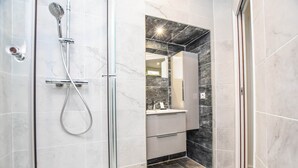 A modern bathroom with a shower, vanity, and marble tiles. - Cosy apartment - 1BR/4P - Auteuil (Paris)