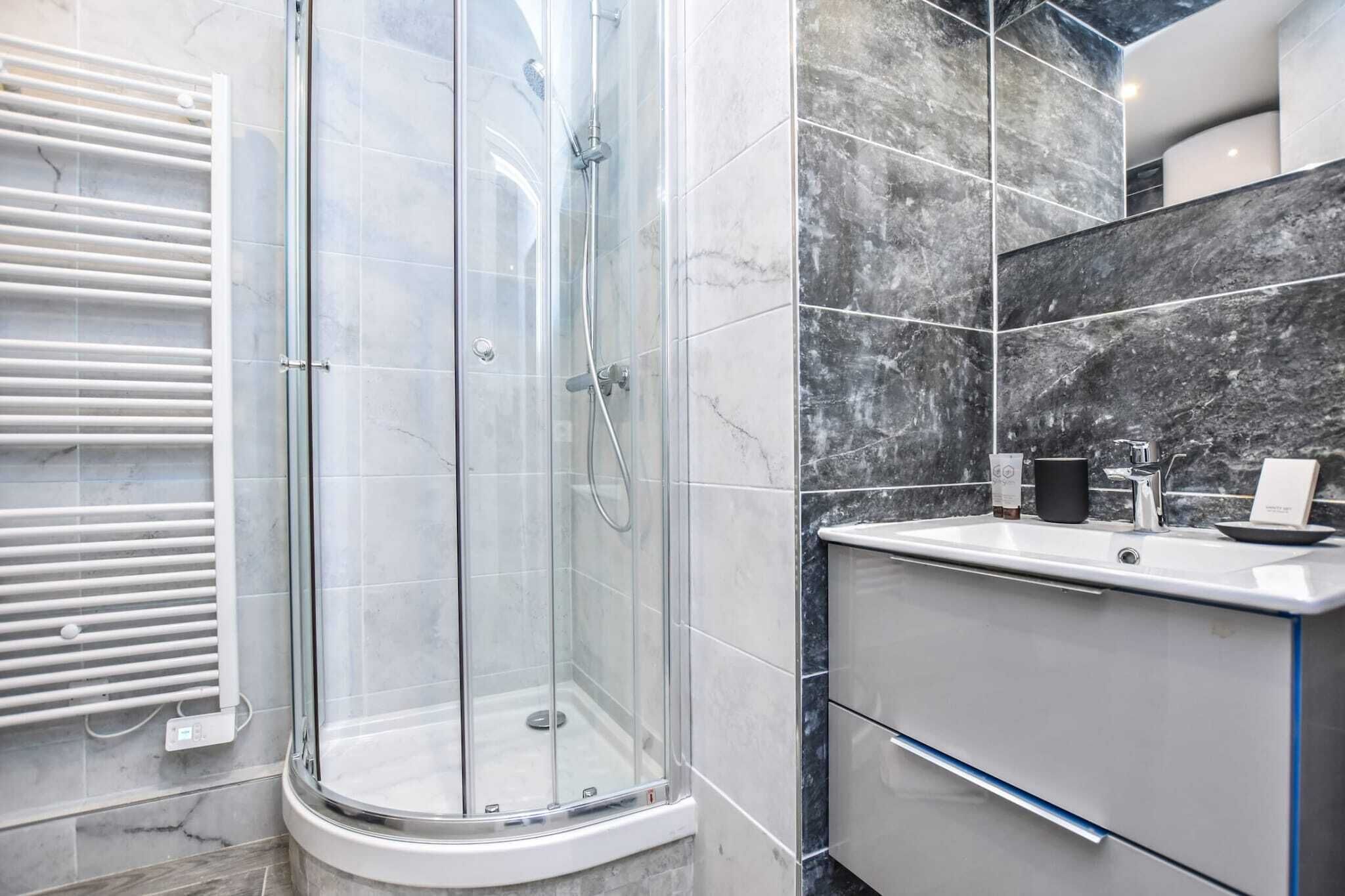 Une salle de bain moderne avec une douche en verre, un lavabo blanc et un mur recouvert de carreaux de marbre.