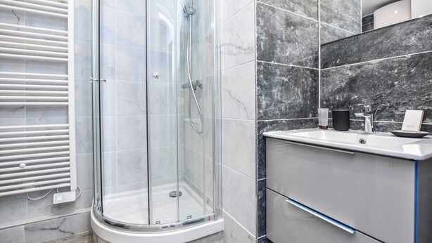 Ein modernes Badezimmer mit einer Duschkabine aus Glas, einem weißen Waschbecken und einer Wand mit Marmorplatten.