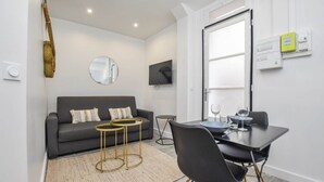 A modern living room with a grey sofa, a round mirror, a flat-screen TV, and a dining area with a table and chairs. - Cosy apartment - 1BR/4P - Auteuil (Paris)