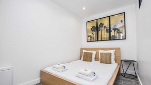 A modern hotel room with a wooden bed, white linens, and a painting of palm trees. - Cosy apartment - 1BR/4P - Auteuil (Paris)