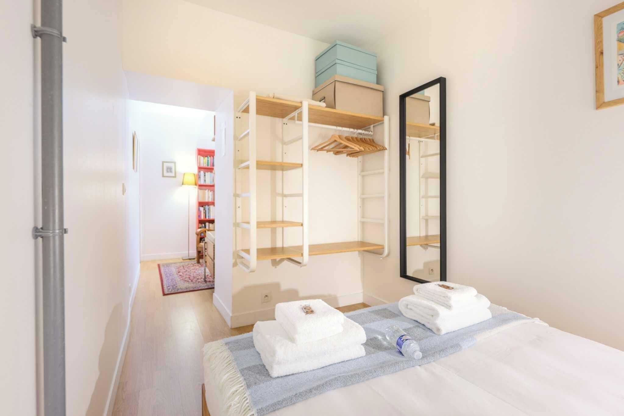 A bedroom with a bed, a wardrobe, a mirror, and a bathroom visible in the background.