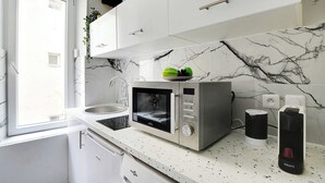 A modern kitchen with white cabinets, a marble backsplash, a built-in microwave, and a window. - Cozy Studio in the heart of the Marais (Paris)