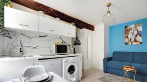 A modern kitchen with white cabinets, a marble backsplash, and a washing machine. - Cozy Studio in the heart of the Marais (Paris)