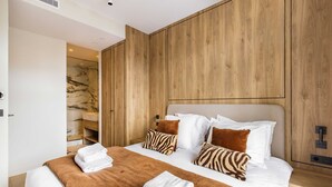 Ein modernes Hotelzimmer mit einem großen Bett, Holzvertäfelung, Marmor-Akzenten und einem Badezimmer mit einer Marmordusche.