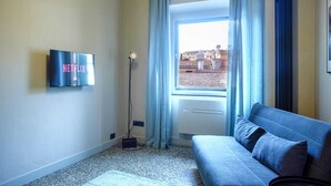 Una habitación con una televisión montada en la pared, una ventana con cortinas, un sofá y un radiador.