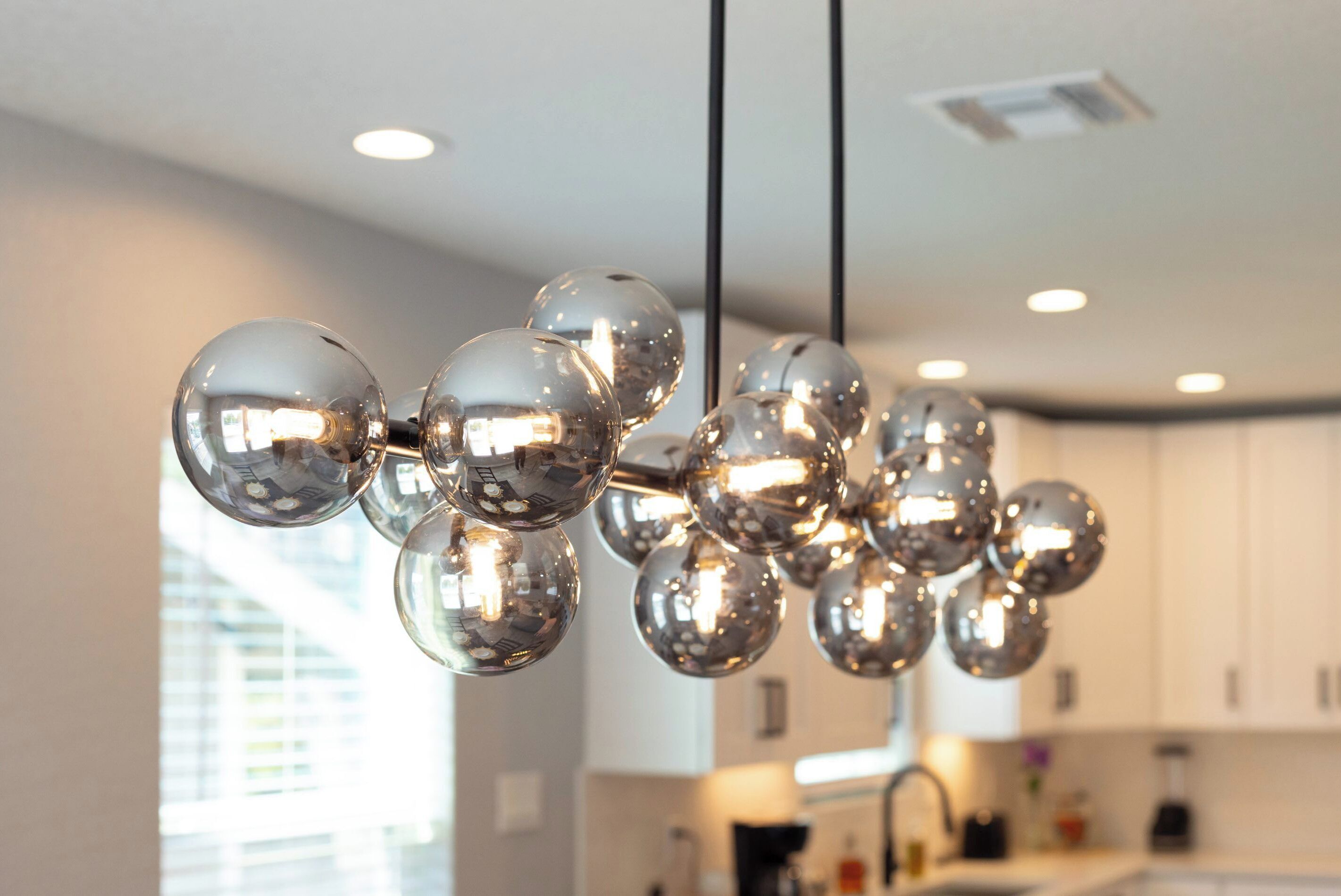 A modern kitchen with white cabinets, a black countertop, and a hanging spherical light fixture.