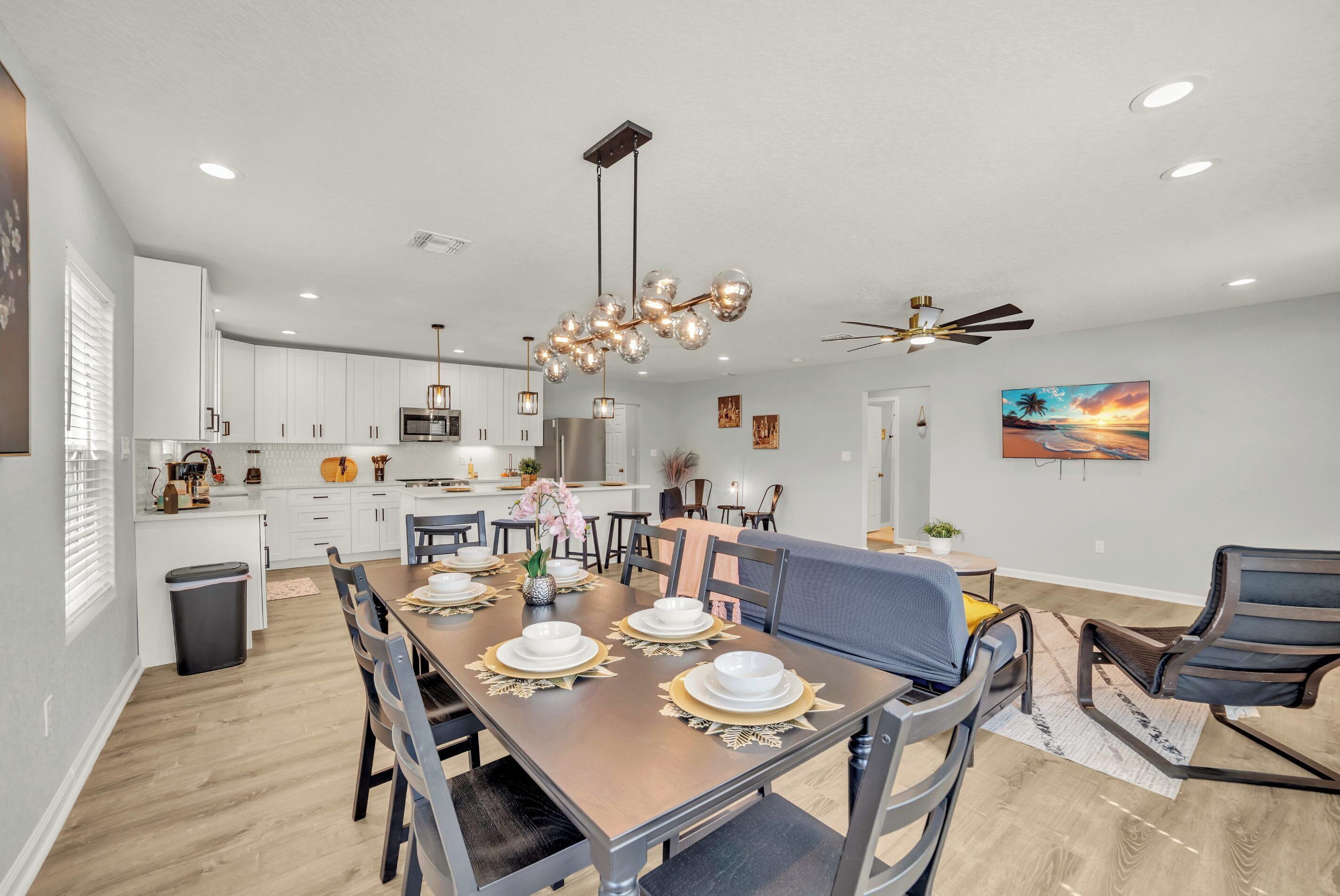 A modern kitchen with white cabinets, a central island, and a dining area with a wooden table set for four.