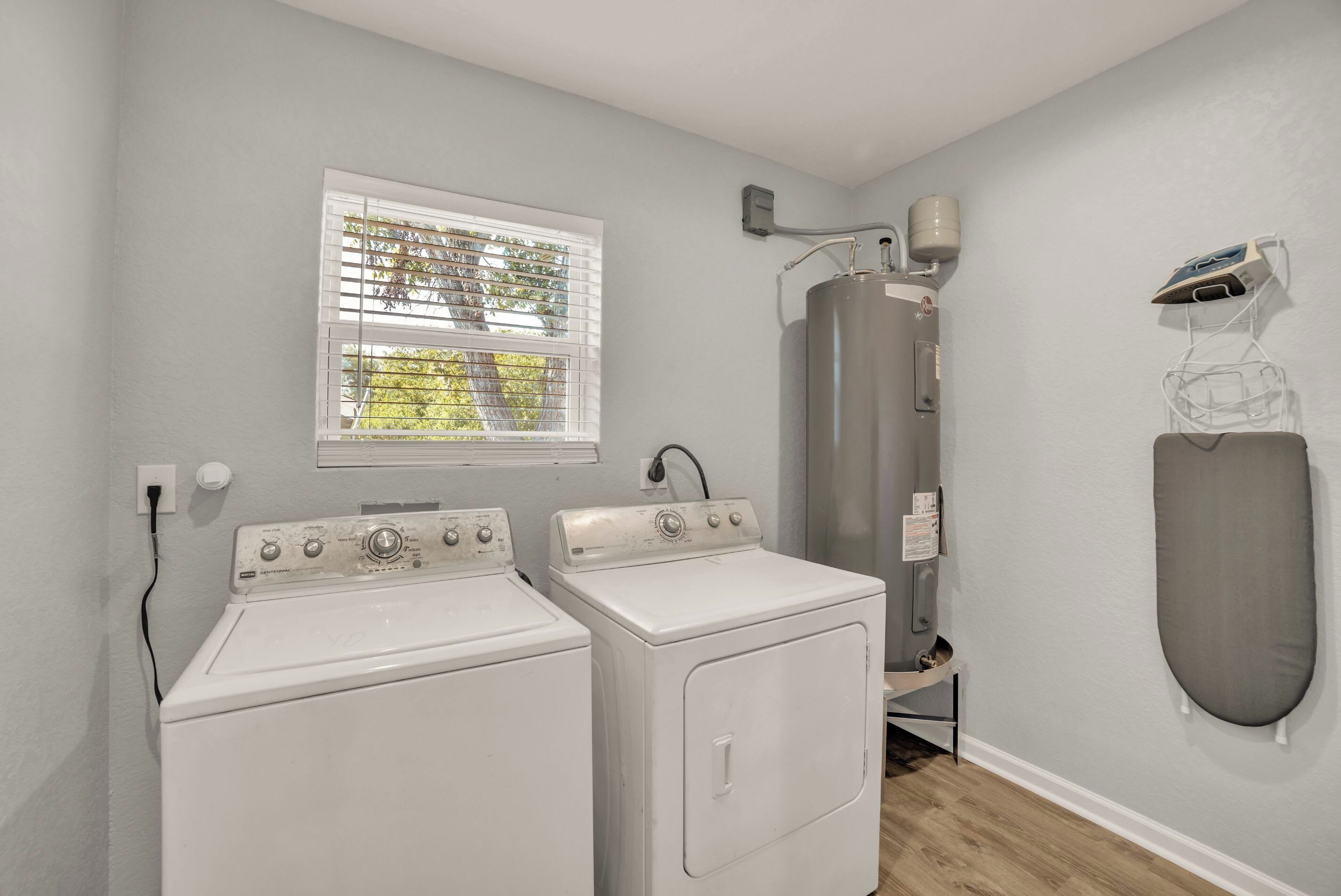 A laundry room with two white front-loading washers and dryers, a water heater, and a wall-mounted ironing board.