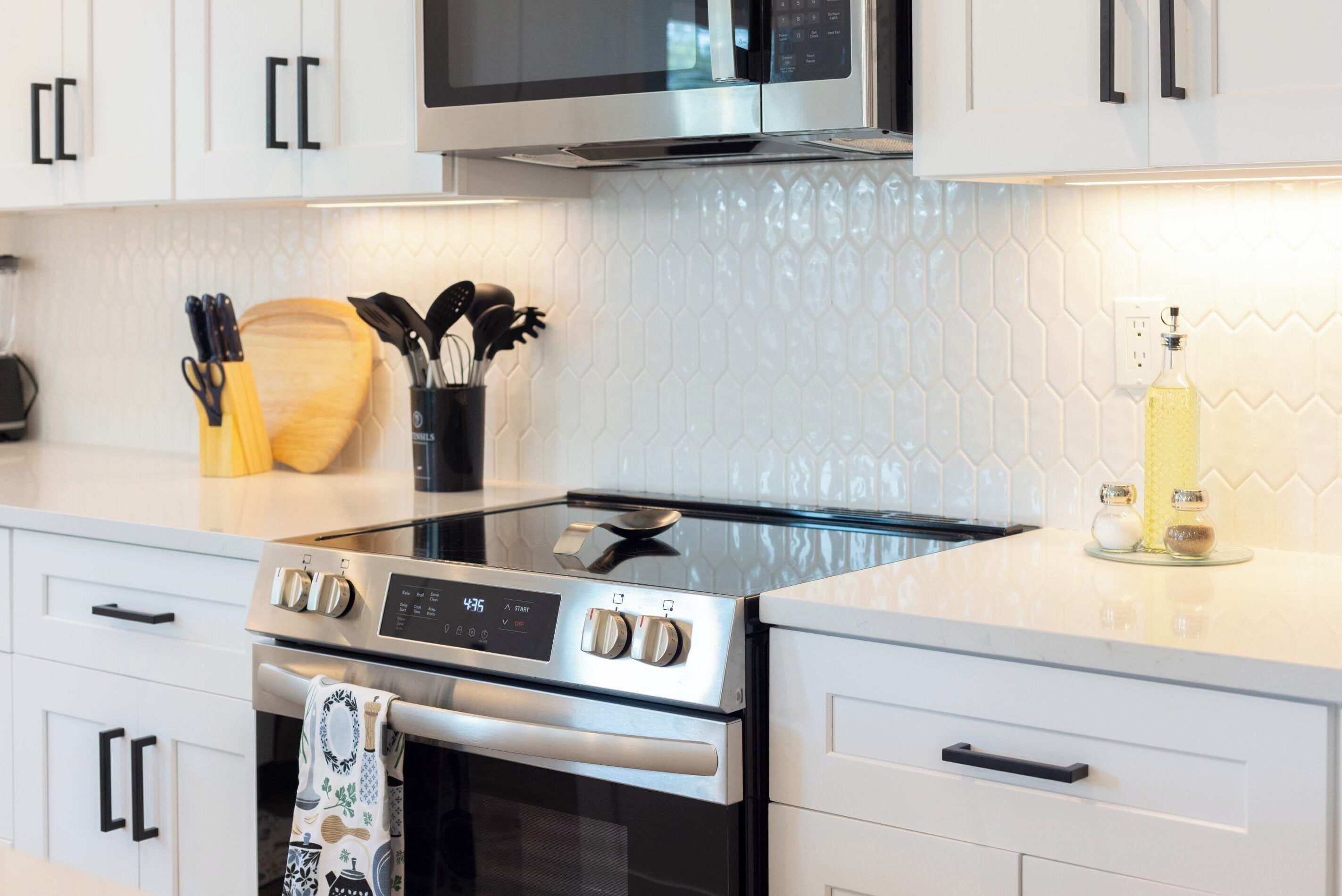 A modern kitchen with stainless steel appliances, white cabinetry, and a hexagonal tile backsplash.