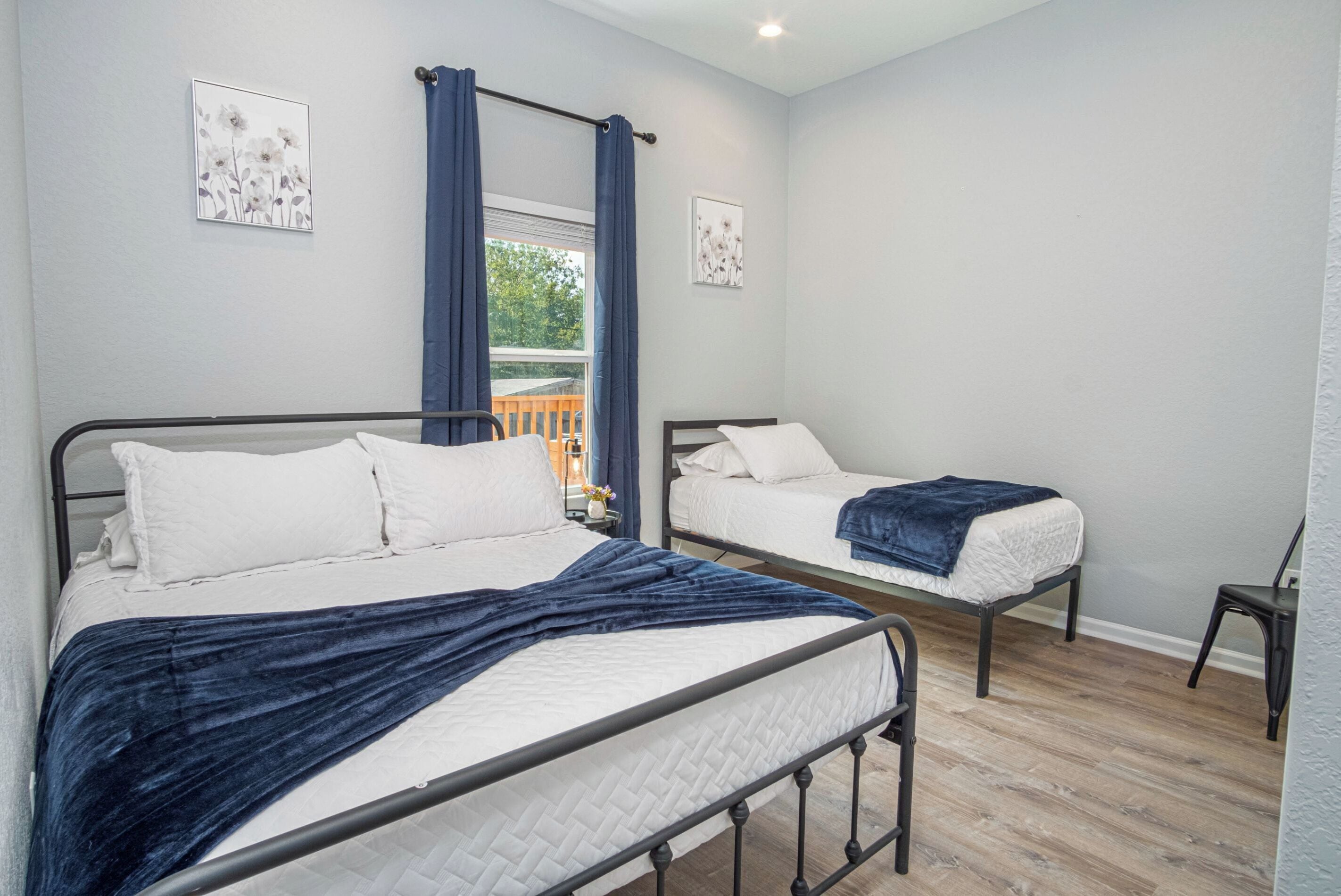 A bedroom with two beds, a window with curtains, and a wooden floor.