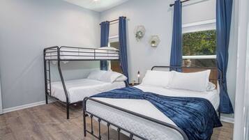Een kamer met twee stapelbedden, een raam met gordijnen, een klein tafeltje met een lamp en een wandplank met planten.