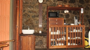A bathroom with a stone wall, wooden cabinets, a sink, a clock, and a cabinet with glass doors containing toiletries.