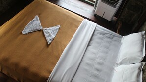 A bed with a brown blanket and white bedding, a white pillow, and a white pillowcase.