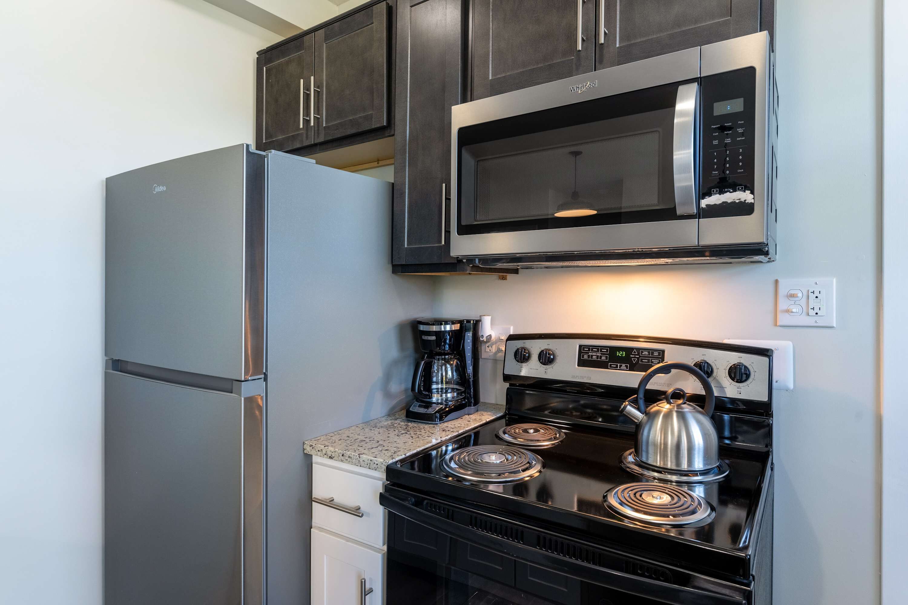 A compact kitchen with a stainless steel refrigerator, a microwave, and a black stove with a kettle.