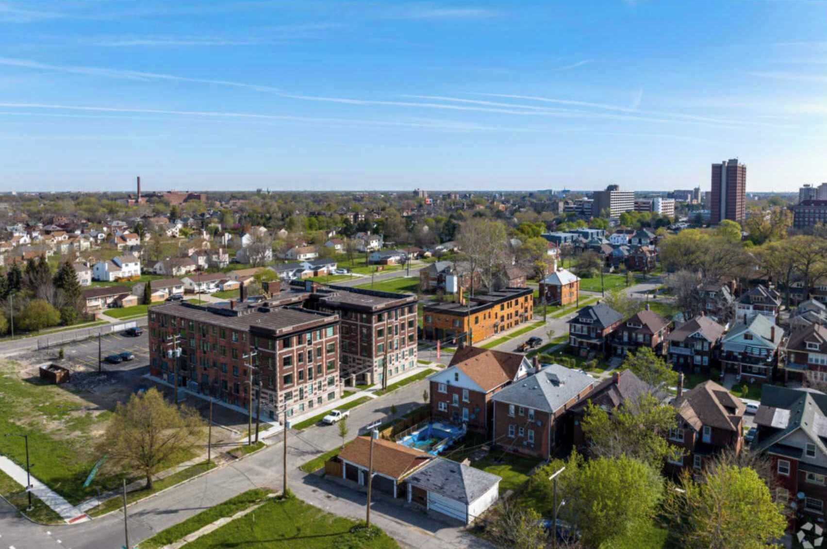 A residential area with a mix of single-family homes and multi-story apartment buildings, featuring a central road and green spaces.