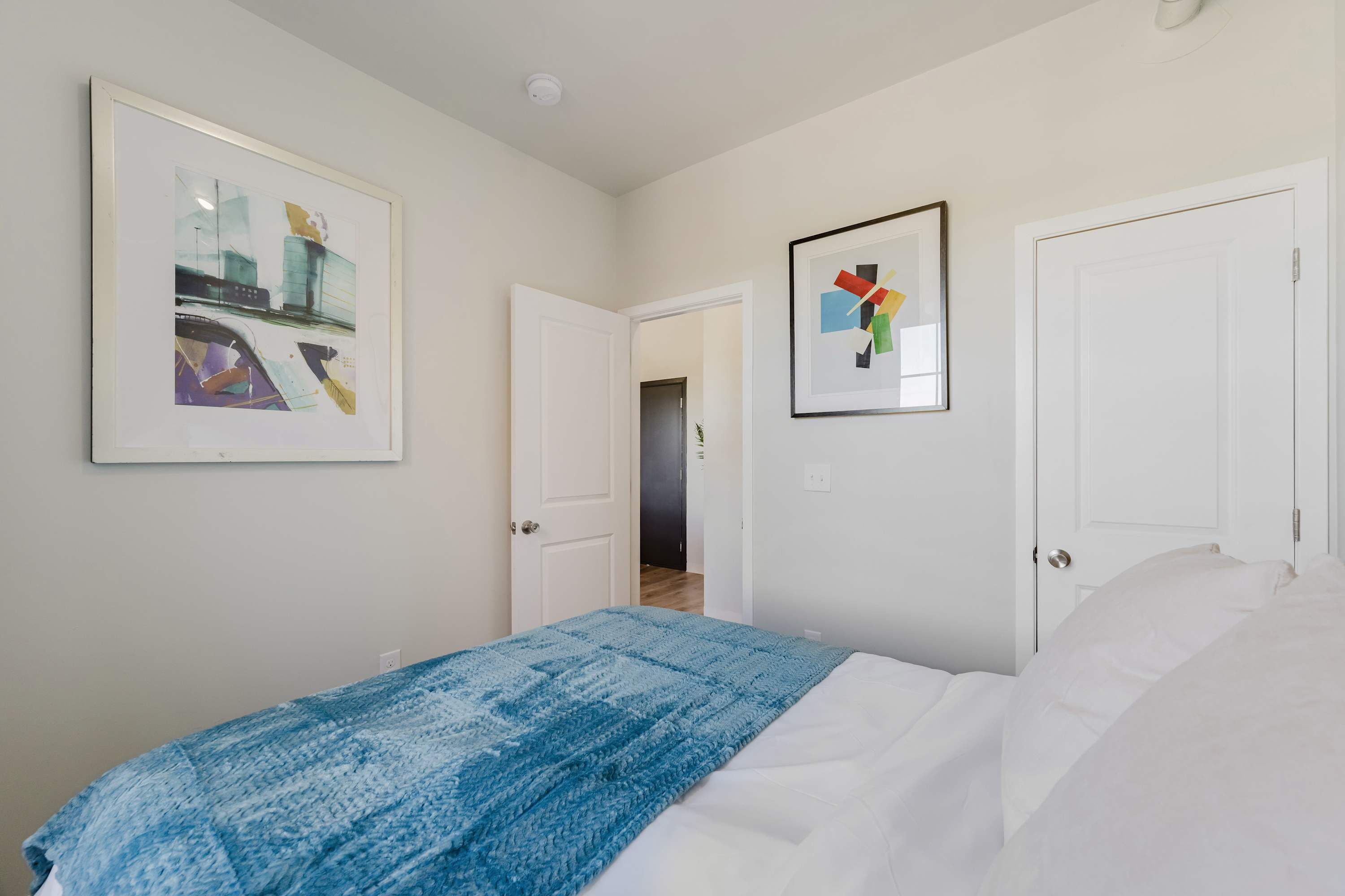 A bedroom with a bed, a blue blanket, and two framed pictures on the wall.