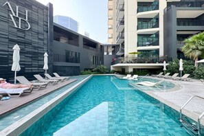 En swimmingpool med liggestole, en moderne bygning med altaner og en klar himmel.