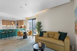 Un salon moderne avec un canapé, un coin repas avec des chaises, une cuisine en arrière-plan et une grande fenêtre.