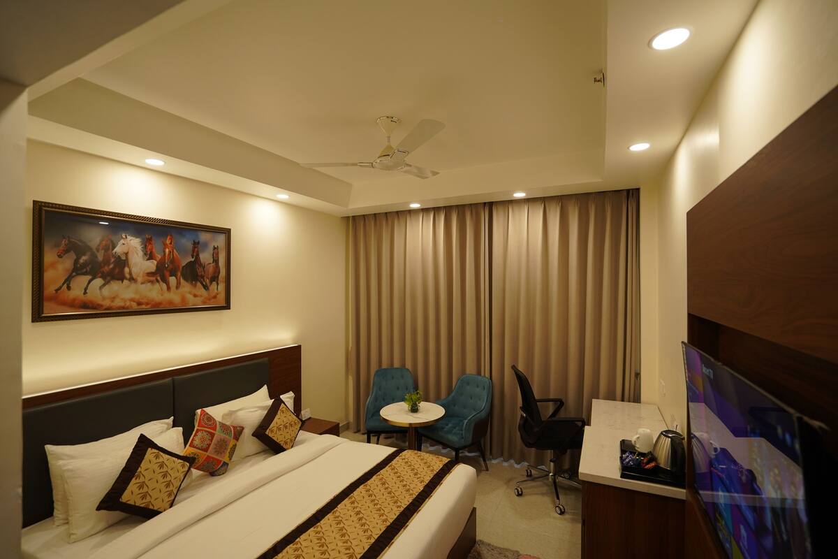 Habitación de hotel con cama, escritorio, silla, ventilador de techo y un cuadro en la pared.