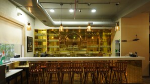 A bar area with a long counter, multiple stools, and hanging light fixtures. - Hotel Luxe Opera NH8 - 7km from IGI Delhi Airport (New Delhi)
