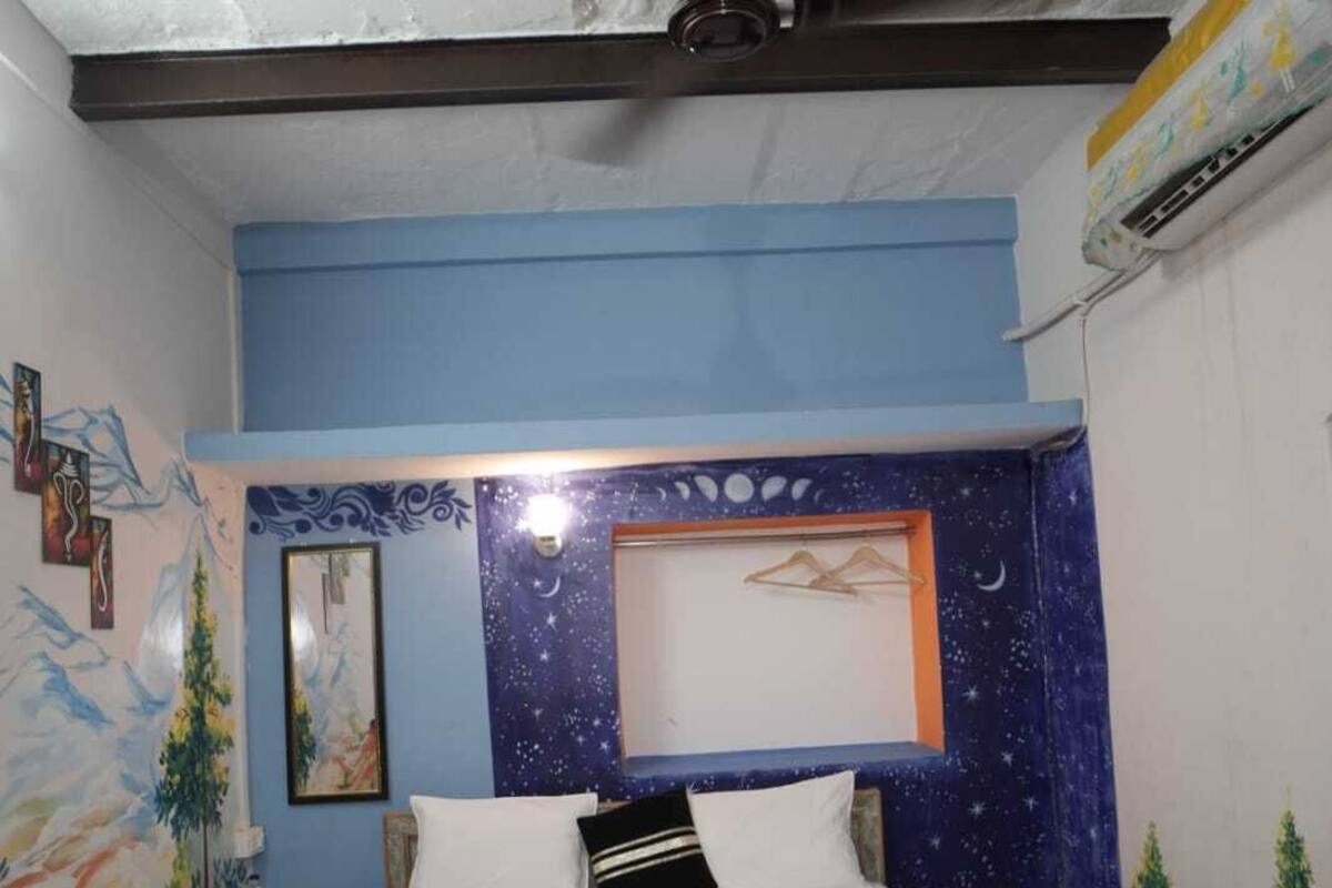Une chambre à coucher avec un lit, un ventilateur de plafond et un mur orné d’une fresque représentant un ciel étoilé.