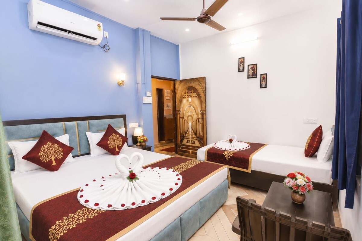 Ein Hotelzimmer mit einem Bett, einem Schreibtisch und einem Stuhl. Es gibt einen Deckenventilator, eine Klimaanlage und ein dekoratives Wandbild.