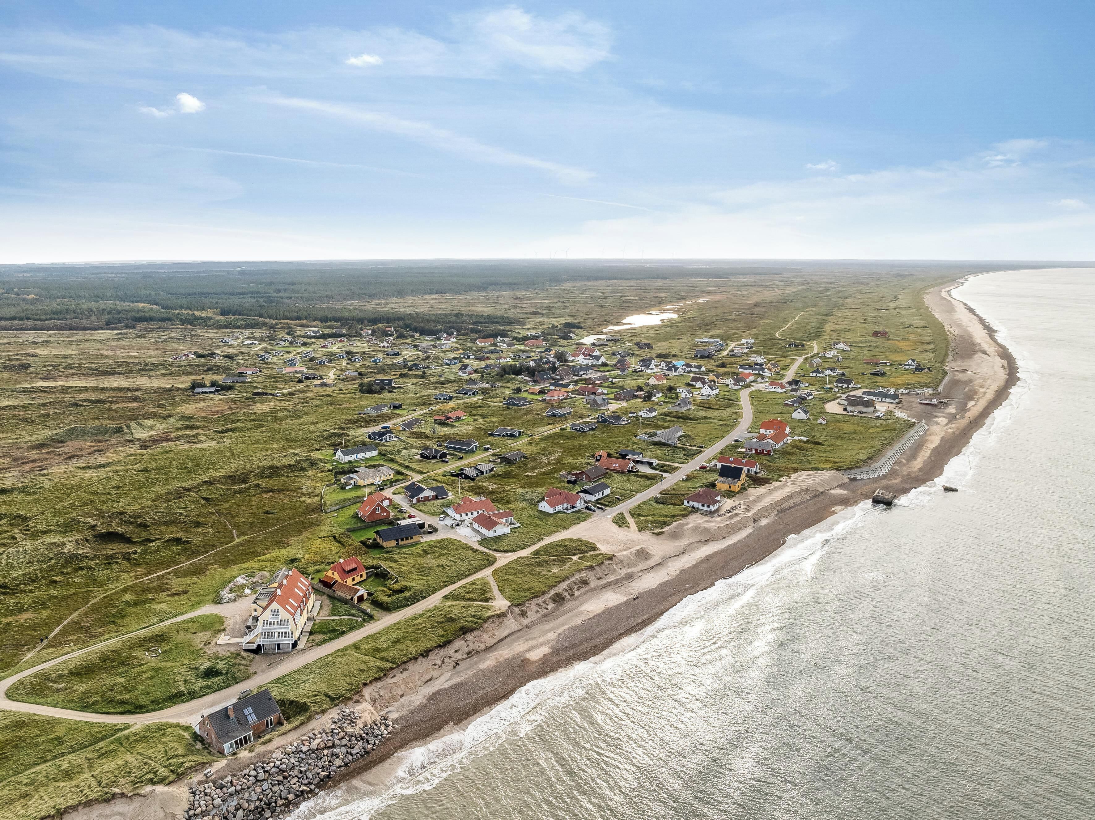 Luftaufnahme eines Küstendorfes mit Häusern entlang des Strandes und einer großen Wasserfläche.