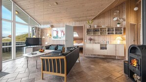 Een moderne woonkamer met een bank, salontafel en televisie. Er zijn grote ramen, houten wanden en een open haard.