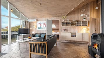 En moderne stue med sofa, sofabord og fjernsyn. Stuen har store vinduer, trævægge og en pejs.