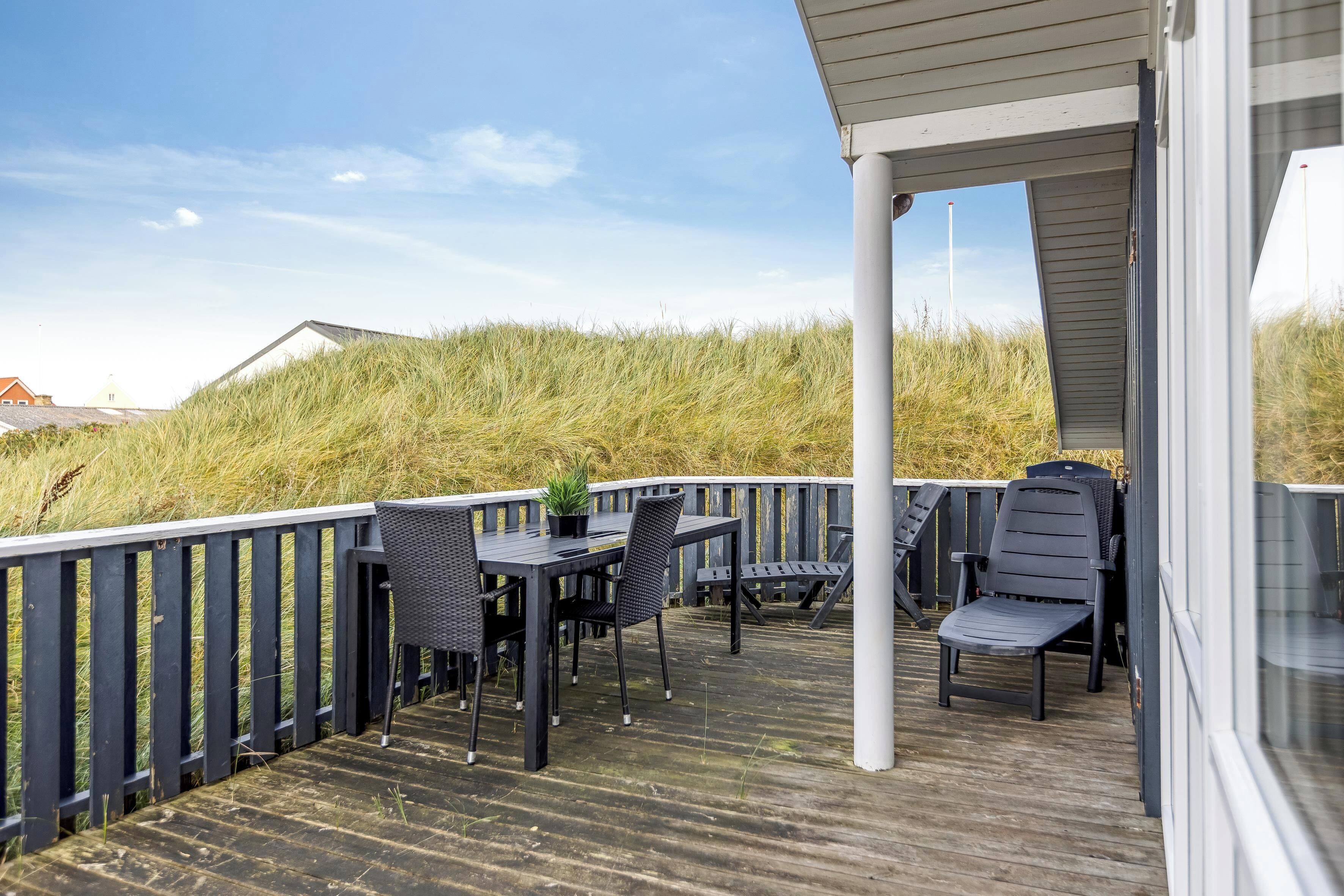 A wooden deck with a table and chairs, overlooking a grassy area.