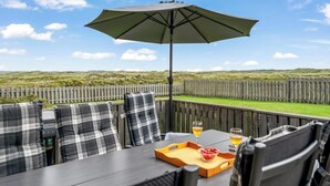 Een terras buiten met een tafel, stoelen, een grote parasol en uitzicht op een gazon.