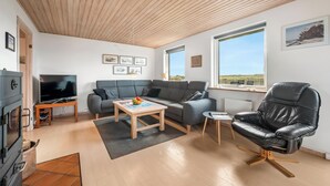 Een moderne woonkamer met een houten plafond, een grijze bank, een zwarte leren fauteuil, een houten salontafel en een televisie.
